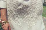 Product picture of the bottom part of the hand embroidery of the Cocoon Coley Barong Tagalog.  Also pictured is Coley's right arm and hand with three brass bangles