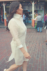 Side view of Jeri walking on a brick road in her dress length hand embroidered cocoon Barong Tagalog. There are people and shops to Jeri's left