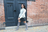 Kristina walks on the sidewalk in front of iron doors and brick walls. Kristina wears a hand embroidered piña silk Barong Tagalog, black tank top underneath barong, black perforated leather miniskirt, gold bracelets on each wrist and suede lavendar thigh high boots