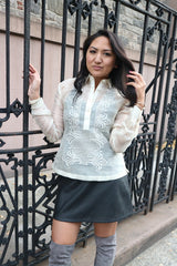 Kristina stands next to a black iron gate and touches one of the bars with her right hand. Her left hand holds and brushes her hair. Kristina wears a hand embroidered piña silk Barong Tagalog, black tank top underneath barong, black perforated leather miniskirt, gold bracelets on each wrist and you can see only the tops of her suede lavendar thigh high boots