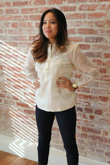 Angled shot of Krizia standing in front of a brick wall with her hands holding each side of her waist. She wears a hand embroidered jusi Barong Tagalog, watch and tight black pants