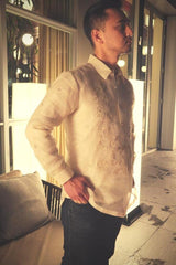 Angled photo of Mansour standing in his hand embroidered piña silk Barong Tagalog. He also wears dark jeans, and he has his hands in his front pockets. Mansour stands in front of a couch with windows, tube light lamps and glass windows and doors in the background