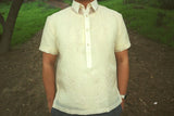 Product picture of the short sleeve hand embroidered cocoon Marc Barong Tagalog. Marc wears a chamisa de chino underneath his barong, a wrist watch and grey pants. Marc has his hands in his pockets. There is a hill trail, grass and a tree in the background