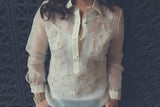 Product photo of the hand embroidered piña silk Roe Barong Tagalog. Roe wears a white tank top underneath her barong. She also wears a necklace underneath her barong and a gold bracelet on her right wrist. There is a decorative iron vent behind Roe