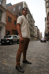Upward photo of Ryan standing on a cobblestone road with parked cars, buildings and a view of the rest of street behind him. Ryan wears a short sleeve hand embroidered jusi Barong Tagalog, a chamisa de chino underneath his barong, brown slacks and dark brown shoes