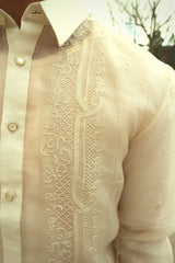 Closeup shot of the upper right calado hand embroidery on the cocoon Ryan Barong Tagalog. Ryan wears a chamisa de chino underneath his barong. There is a tree, building and the sky in the background