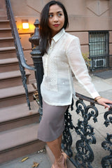 Side view of Jenny in her hand embroidered piña silk Barong Tagalog, grey tank top underneath the barong, grey skirt, and pink open to shoes. Jenny stands with her left knee bent and left hand on the black iron decorative gate she leans back on. She stands looking to her left. There are stairs and a brownstone house to her right