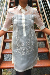 Product picture of the dress length hand embroidered cocoon Bianca Barong Tagalog with red stairs behind her 