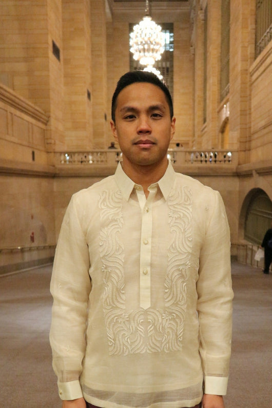 Photo from waist up of Blase in his hand embroidered piña silk Barong Tagalog  in Grand Central Terminal in NYC with beige walls and chandelier behind him