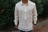 Product shot of the hand embroidered piña silk Bryan Barong Tagalog. Bryan wears blue jeans and a black wrist watch, and he stands on a brick walkway with dead leaves on the ground and multiple groups of green shrub leaves behind him