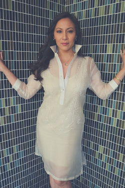 Jeri stands in the corner of two multicolor tile walls with her hands resting on the wall. Jeri wears her dress length hand embroidered cocoon Barong Tagalog, a beige minidress underneath her barong, hoop earrings, heart pendant necklace, gold bangles and diamond ring on her left arm and hand 
