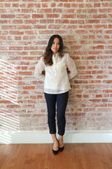 Full body picture of Krizia. She stands on a wood floor with her back to a brick wall. Her hands are behind her back. She wears a hand embroidered jusi Barong Tagalog, tight black pants and black pointed shoes.