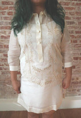 Product shot of the hand embroidered jusi Krystal Barong Tagalog. There is wood flooring, white base boards and a brick wall in the background