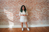 Krystal stands in front of a brick wall in her dress length hand embroidered jusi Barong Tagalog. She holds her hands in front of her and is wearing Air Jordan 3 White Cement sneakers and plastic rimmed glasses