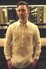 Half body photo of Mansour standing in his hand embroidered piña silk Barong Tagalog. Mansour stands in front of a bar and mirrors. His hands are over his front jeans pockets.