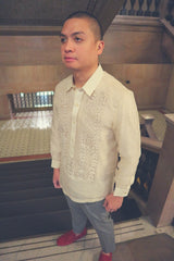 Angled picture of Mark in his hand embroidered piña silk Barong Tagalog, grey slacks and red loafers. He stands at the top of a flight of black stairs. There are light grey marble walls, bannisters, and the lower floor in the background