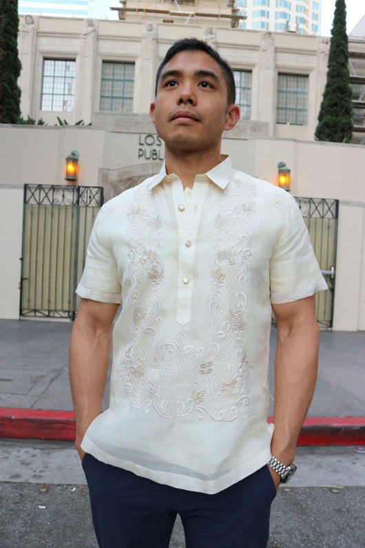 Matt stands in front of the Los Angeles Public Library in his short sleeve hand embroidered jusi Barong Tagalog. Matt also wears a chamisa de chino underneath his barong, blue pants and a wrist watch on his left wrist. The road, sidewalk, gates and trees are also in the background