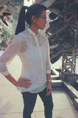 Michelle stands at an angle with her right hand on her right hip. She stands in front of a metal component sculpture in downtown Los Angeles. Michelle wears a hand embroidered piña silk Barong Tagalog, a white tank top underneath the barong, green pants, brown glasses and a watch and ring on her left wrist and hand.