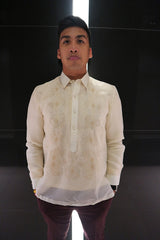 Noel looks straight into camera and stands with his hands in his pockets in front of a black reflective wall with a light strip down the middle. Noel wears a hand embroidered jusi Barong Tagalog, a chamisa de chino underneath his barong, dark maroon slim slacks, a black wrist watch on his left wrist.