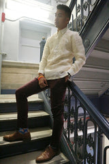 Angled picture of Noel standing and leaning back on a bannister in a stairwell. Noel has his feet on two different steps, his left hand in his pocket and his right hand resting on his right hip. Noel wears a hand embroidered jusi Barong Tagalog, dark maroon slim slacks, blue patterned socks, brown dress shoes, a black wrist watch on his left arm  and yellow and red bracelets on his right wrist