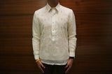 Product photo of the hand embroidered jusi Noel Barong Tagalog. Noel wear a chamisa de chino underneath his Barong Tagalog, dark maroon slim slacks, a black wrist watch on his left wrist, and yellow and red bracelets. Noel stands in front of a brown wood wall.