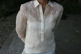 Product photo of the hand embroidered piña silk Robin Barong Tagalog. Robin wears a white tank top underneath her barong. Robin's hands are behind her back. There are concrete and stone walkways and plants in the background