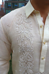 Closeup of the calado hand embroidery on the upper left side of the piña silk Rodrigo Barong Tagalog. Rodrigo wears a chamisa de chino under his barong. Rodrigo stands at the High Line Park in New York City with buildings behind him