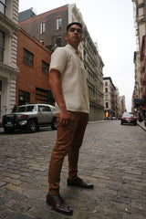 Upward photo of Ryan standing on a cobblestone road with parked cars, buildings and a view of the rest of street behind him. Ryan wears a short sleeve hand embroidered jusi Barong Tagalog, a chamisa de chino underneath his barong, brown slacks and dark brown shoes  