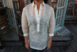 Product photo of the hand embroidered piña silk Sarahlynn Barong Tagalog. Sarahlynn wears a black tank top underneath her barong, and dark blue jeans. Sarahlynn stands on a wooden rooftop deck with a wooden tower with windows behind her