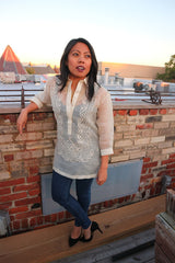Sarahlynn stands in her hand embroidered piña silk Barong Tagalog, black tank top underneath her barong, dark blue jeans, and black high heel shoes. She stands on a wodden plank, leaning back with her right elbow resting on the brick wall behind her. She is on a rooftop, and other rooftops, chimneys, a tree and the sky are in the background