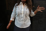 Product photo of the hand embroidered jusi Stephanie Barong Tagalog. Stephanie stands in a black doorway. She wears a black 3/4 sleeve shirt underneather her barong and grey skirt. Stephanie holds her left hand up with palm facing the camera and her right hand extended at her side