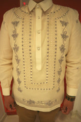 Product photo of the jusi Tonilyn Barong Tagalog. Tonilyn wears a chamisa de chino under the barong, light brown khaki pants and a beaded bracelet on the left hand. There is a red and white wall behind Tonilyn.